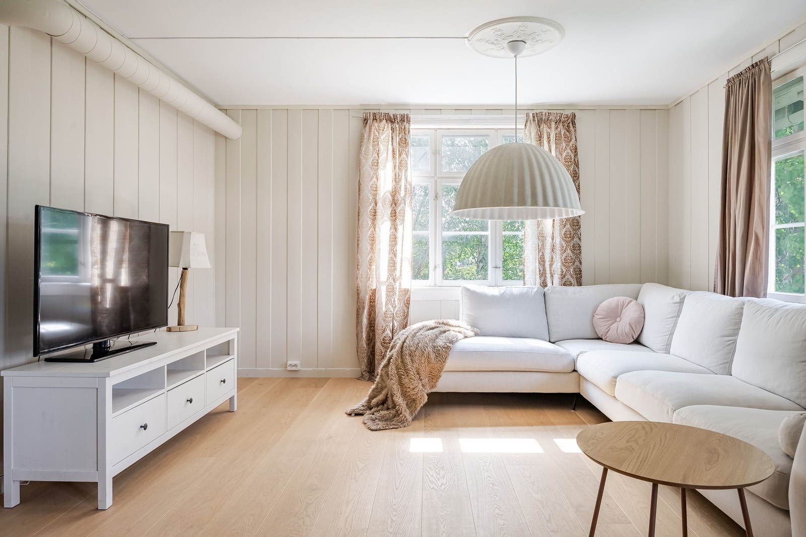 Lys og innbydende stue med store vinduer og i hovedsak malte panelvegger. Galleribilde