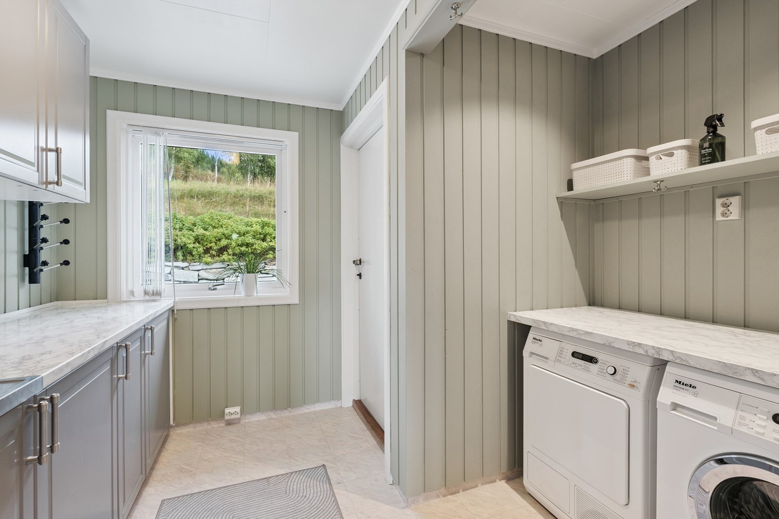 Nær badet ligger boligens praktiske vaskerom med god gulvplass og større skapinnredning på vegg. I en egen nisje finner man vann- og avløpsuttak for vaskemaskin og tørketrommel. På vaskerommet, som har egen utgang til terrasse og videre til terreng. Galleribilde