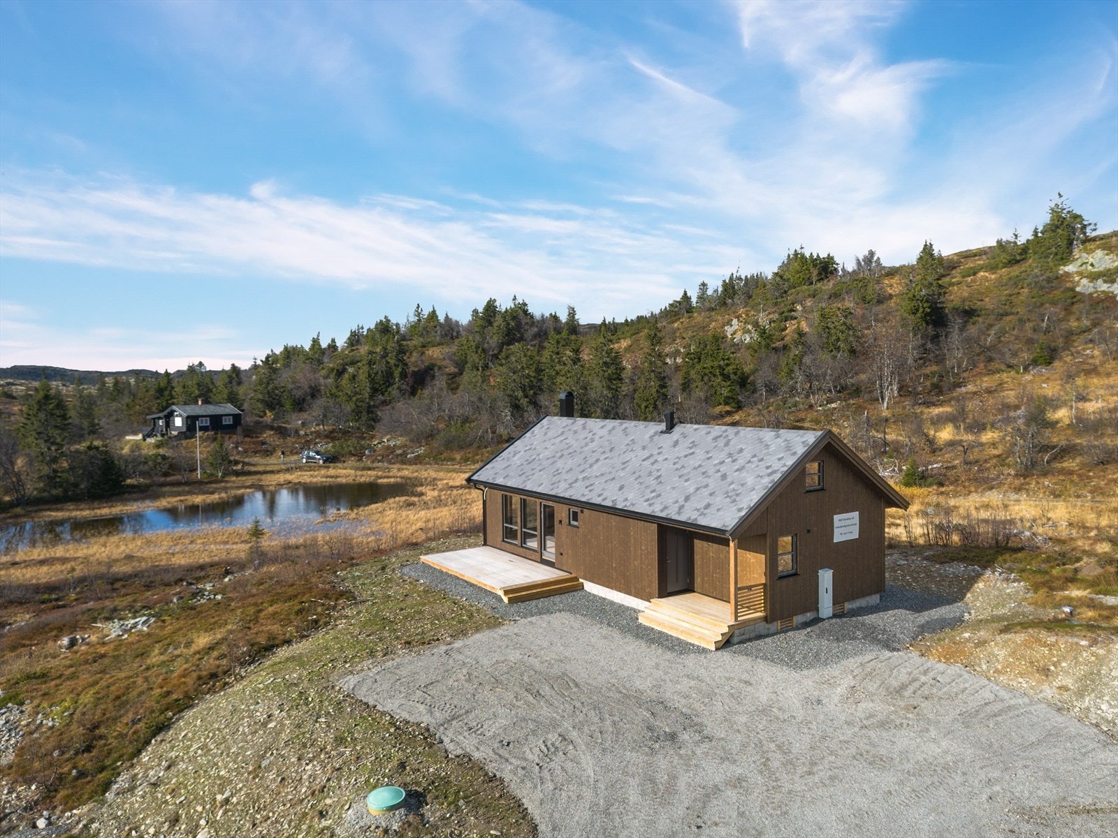 Eiendommen har en romslig naturtomt, og fra den solrike terrassen er det fin utsikt utover området, ikke minst mot det lille tjernet som ligger i nærheten. Det er også plass til en mindre sittegruppe i tilknytning til hyttas overbygde inngangsparti. Galleribilde