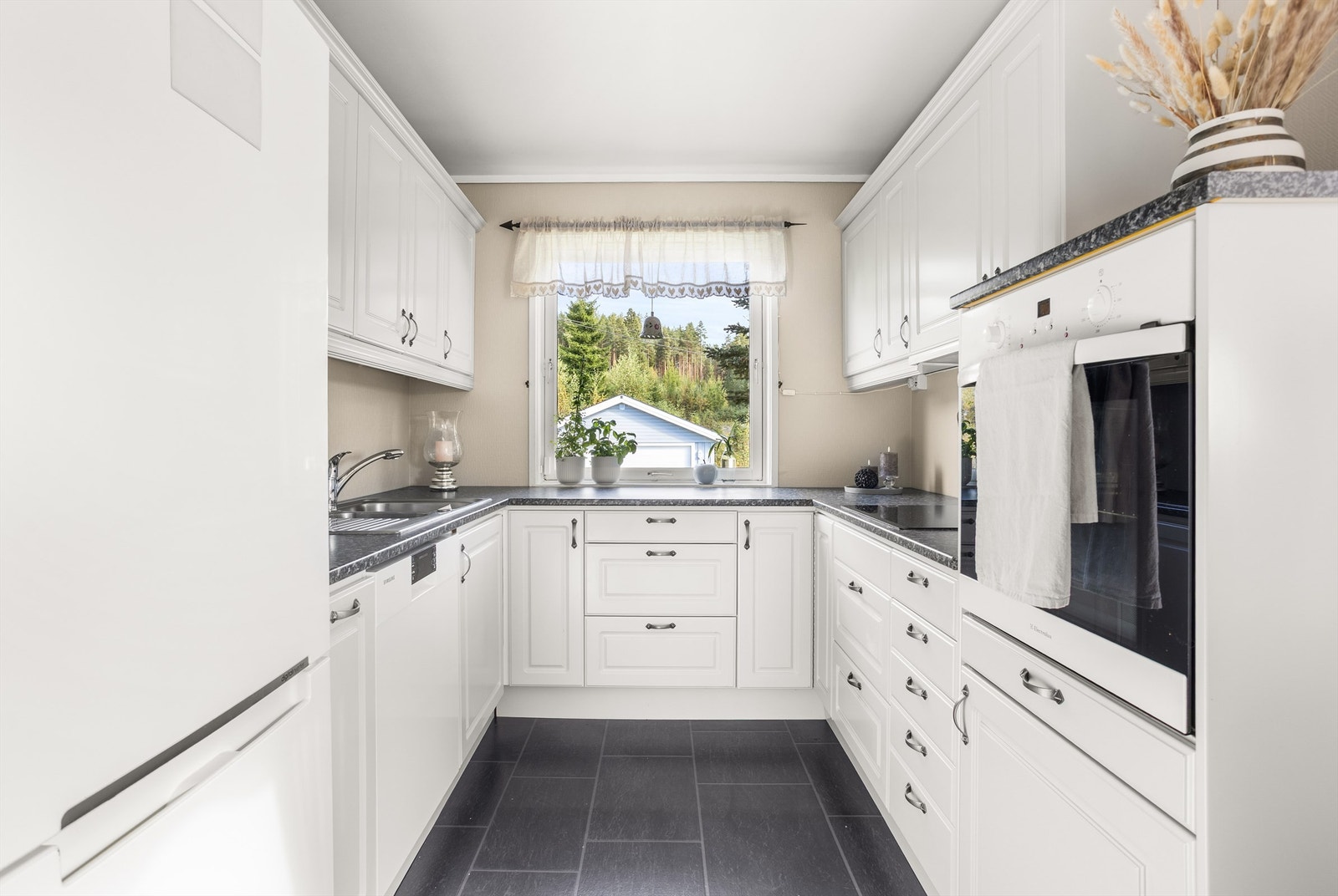 Kjøkken med hvite under og overskap. Det er blandt annet inkludert hvitevarer som oppvaskmaskin, komfyrplate og stekeovn Galleribilde