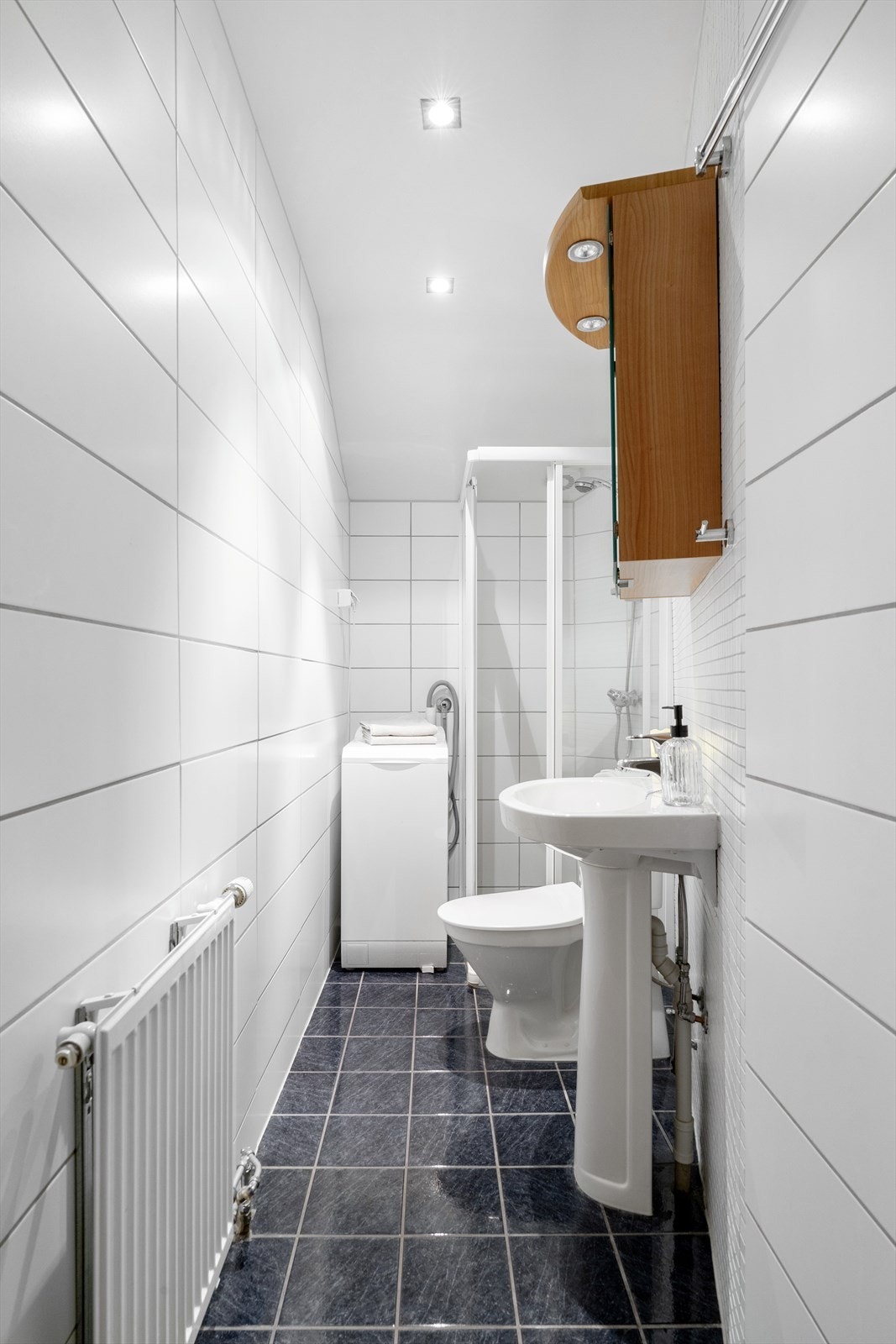 Flislagt bad utstyrt med servant, speilskap, wc, dusjhjørne og opplegg til vaskemaskin. Galleribilde