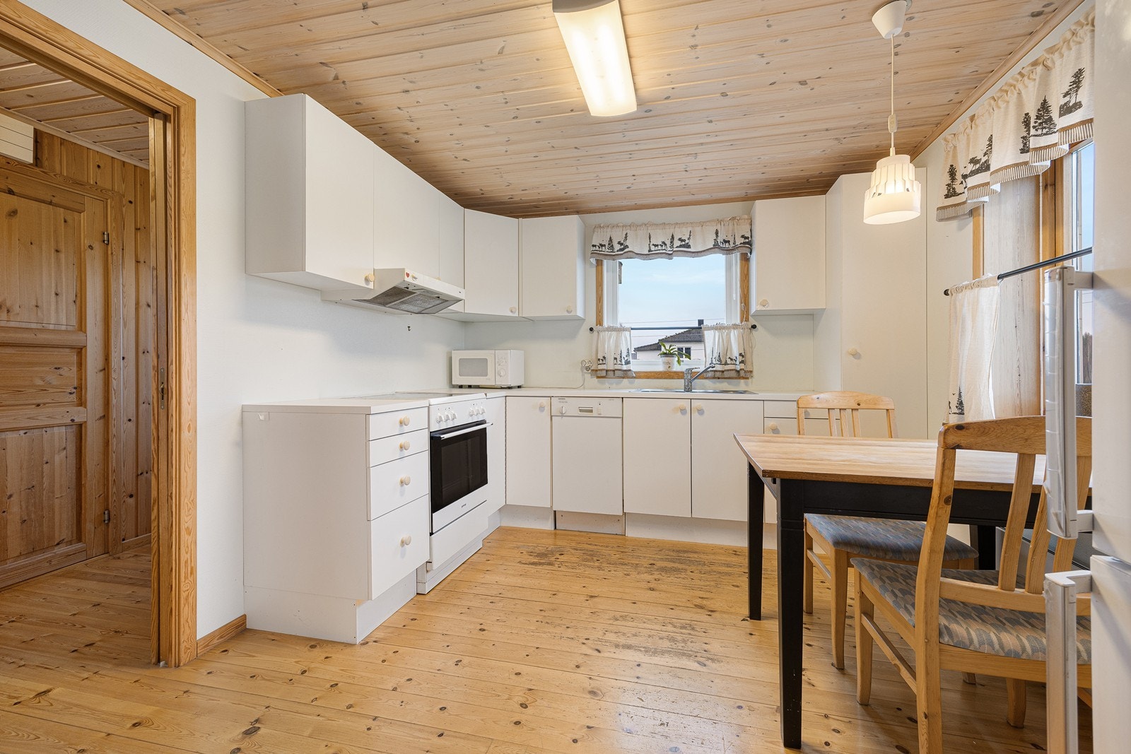 Kjøkkenet ligger i eget rom og har et lyst, tidløst design med hvite, glatte fronter og hvit laminatbenkeplate med nedfelt kum i stål. Galleribilde