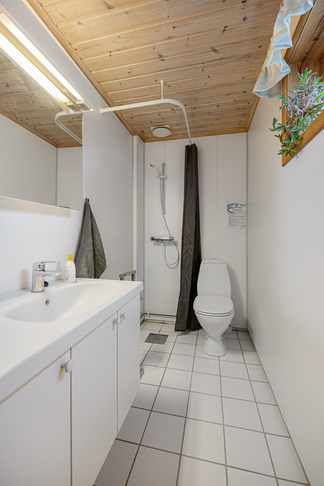 Innredningen på badet i første etasje har heldekkende servant over skapseksjon og speil i overkant. Videre er det gulvmontert toalett og dusjhjørne med veggmontert dusjarmatur. Galleribilde