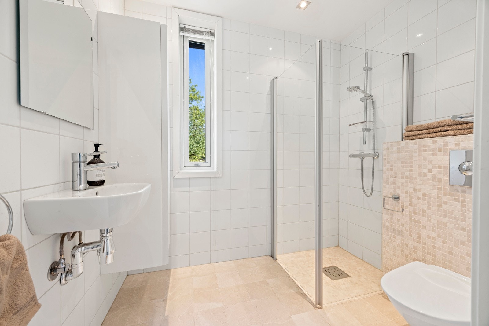 Bad nr. 1. Lyst flislagt baderom innredet med dusjnisje, servant, vegghengt skap og klosett. Galleribilde