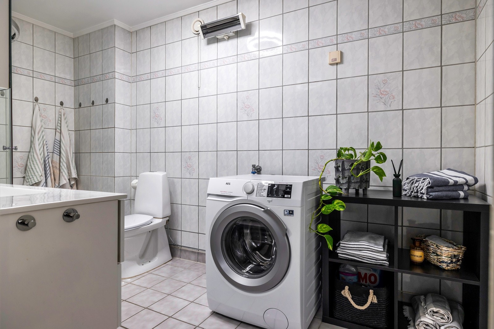 Det er innredet med dusjkabinett med glassdører, servant med skuffer, speilskap med belysning og frittstående toalett. Rommet har også opplegg for vaskemaskin og tørketrommel, og plass til hyller eller skap for ekstra oppbevaring. Galleribilde