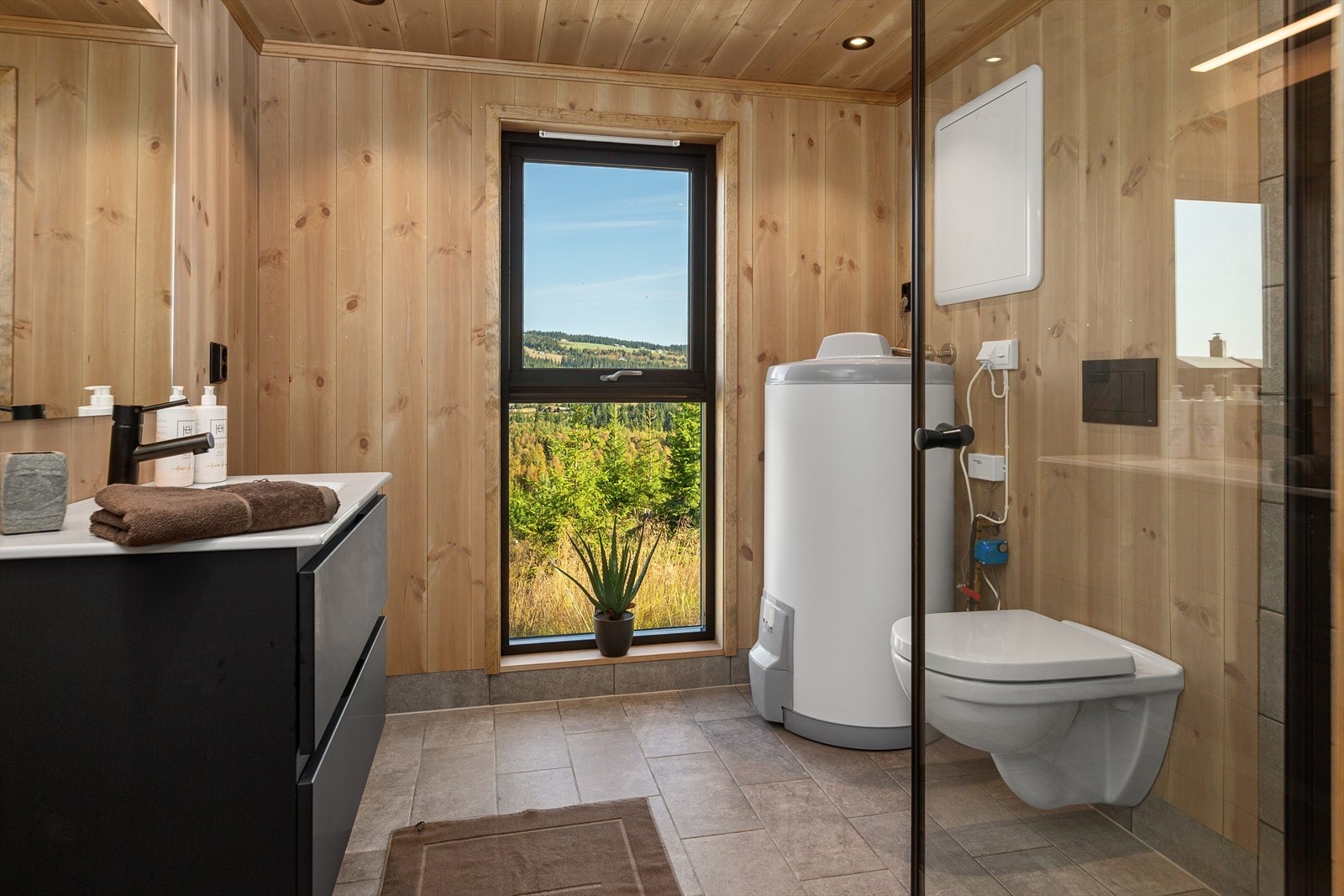 På badet er det lyst og hyggelig med et høyt vindu ut mot ubebygd terreng. Badet har pent flislagt gulv med vamekabler og moderne servantskap med store skuffer og helstøpt servantplate. Galleribilde