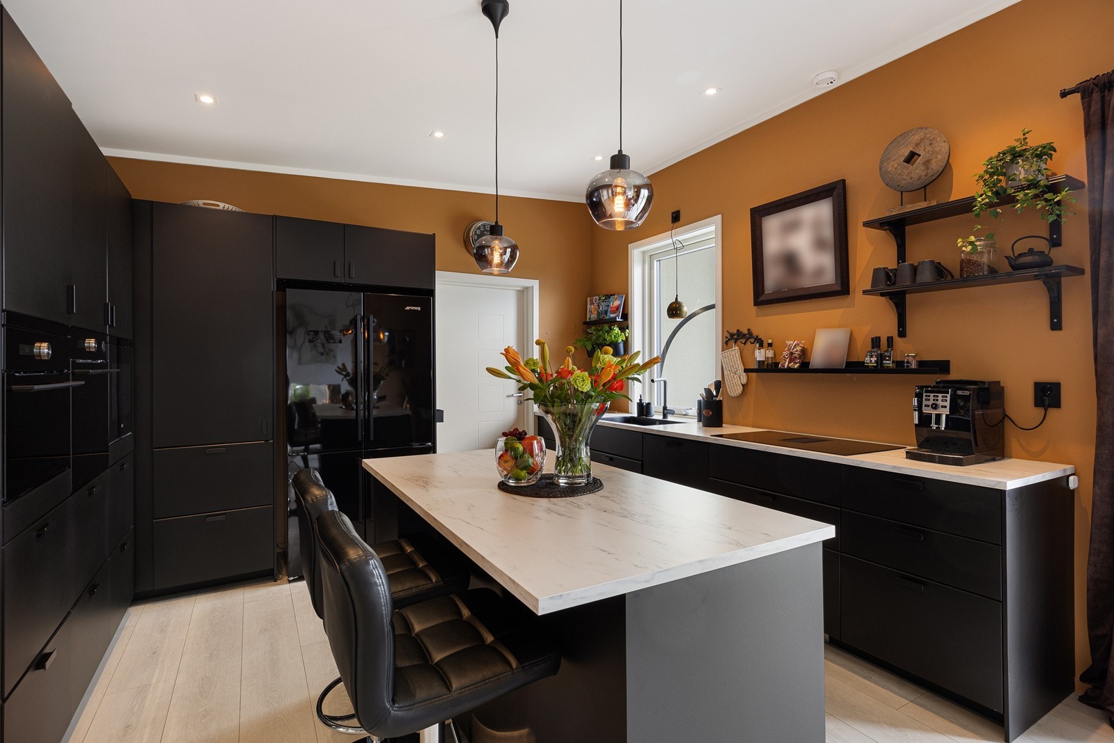 Innredningen har sorte, glatte fronter og lys laminatbenkeplate i marmor-look med sort oppvaskkum. Induksjonstopp med innbebygget ventilator, integrert vinskap, oppvaskmaskin og stekeovn. Galleribilde