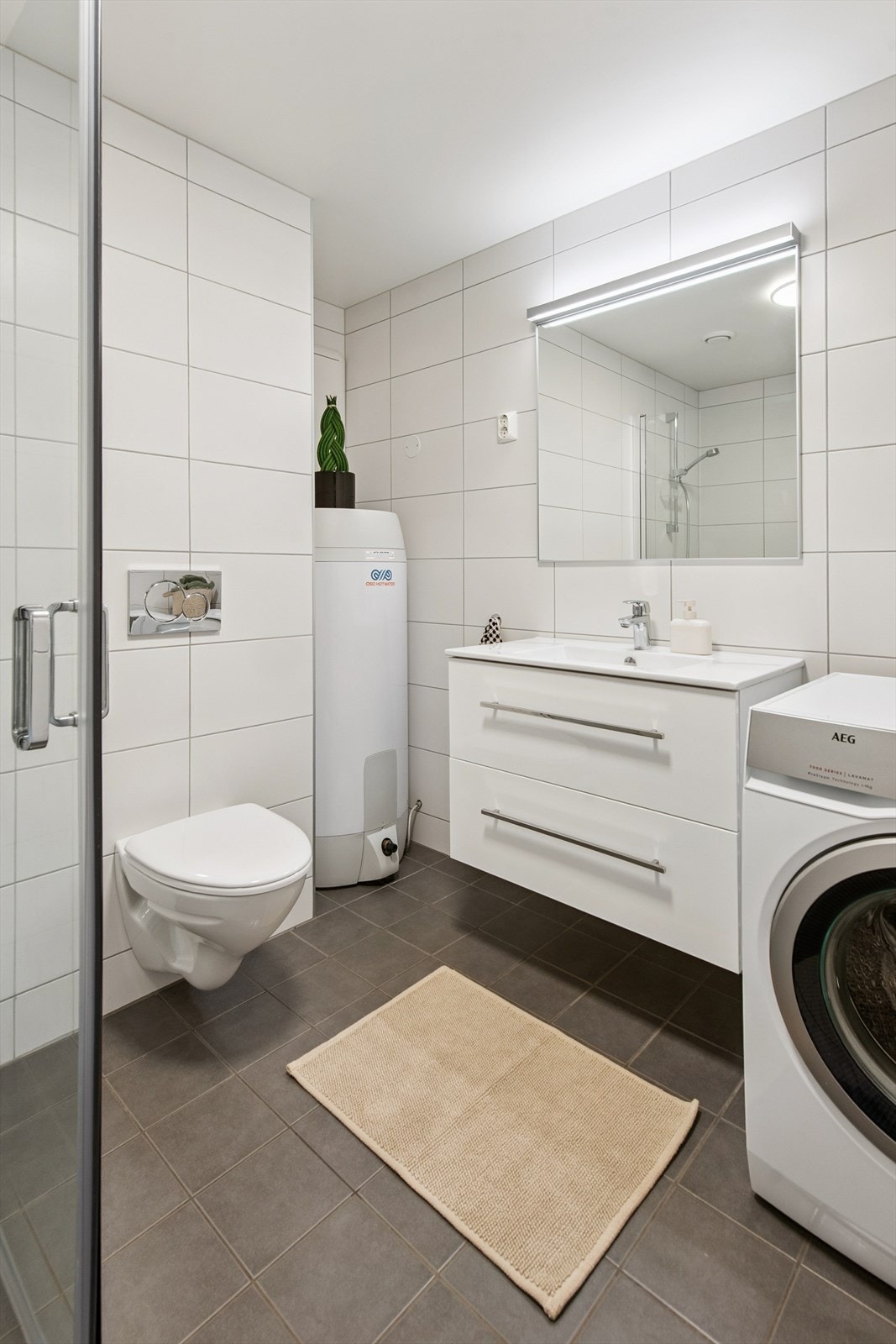 Badet er innredet med servantmøbel, vegghengt toalett og dusjhjørne med glassdører. Galleribilde