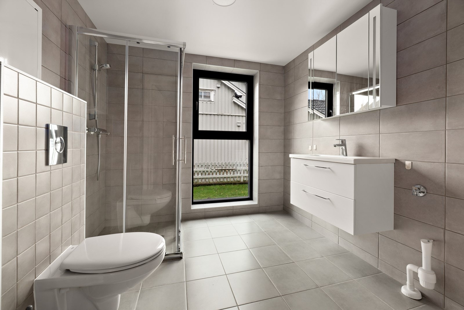 Flislagt flott bad. Dusjhjørne, vegghengt toalett, innredning med store skuffer. Speilskap. Galleribilde