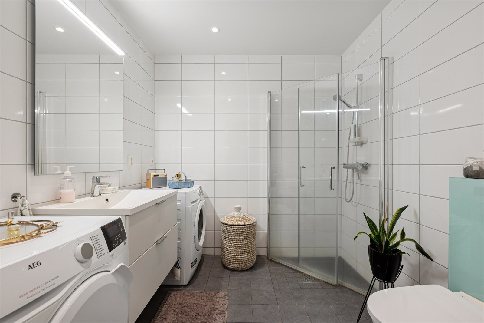 Badet fremstår som lyst og pent, Rommet er innredet med servant, speil m/ belysning, underskap, dusjnisje og opplegg for tørke- vaskemaskin. Galleribilde