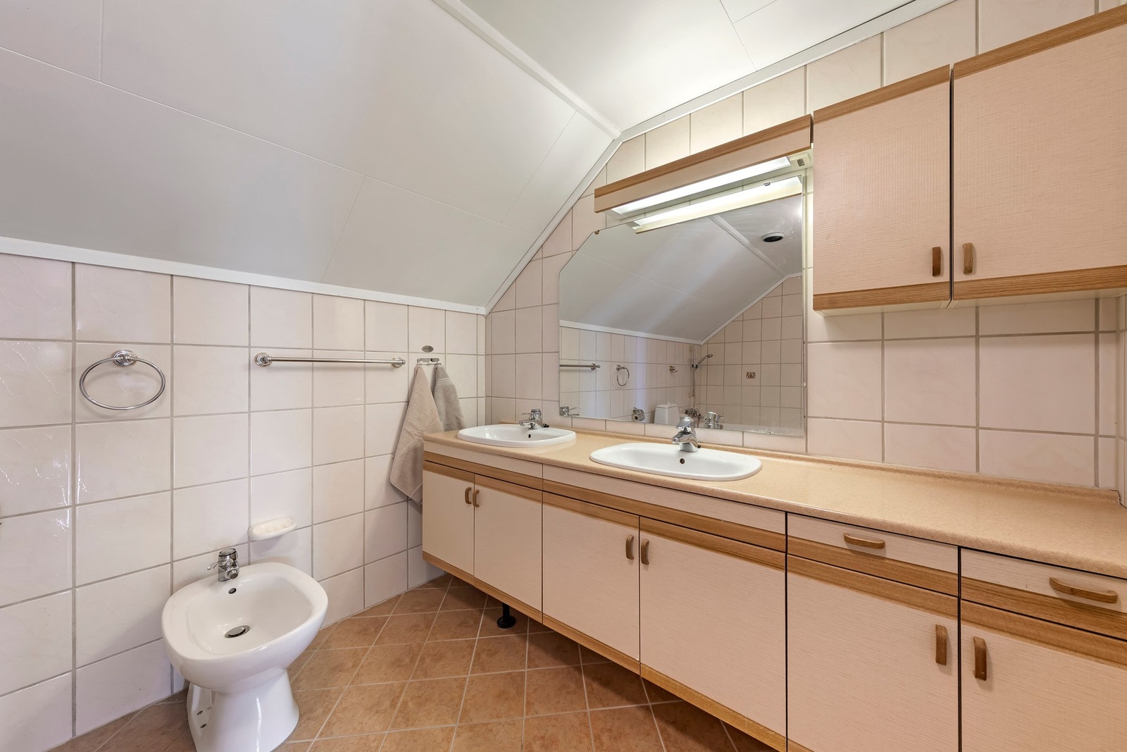 Baderomsinnredning med tredetaljer, laminat benkeplate, overskap og speil. Toalett, bidé, nedfelte servanter og badekar er montert Galleribilde