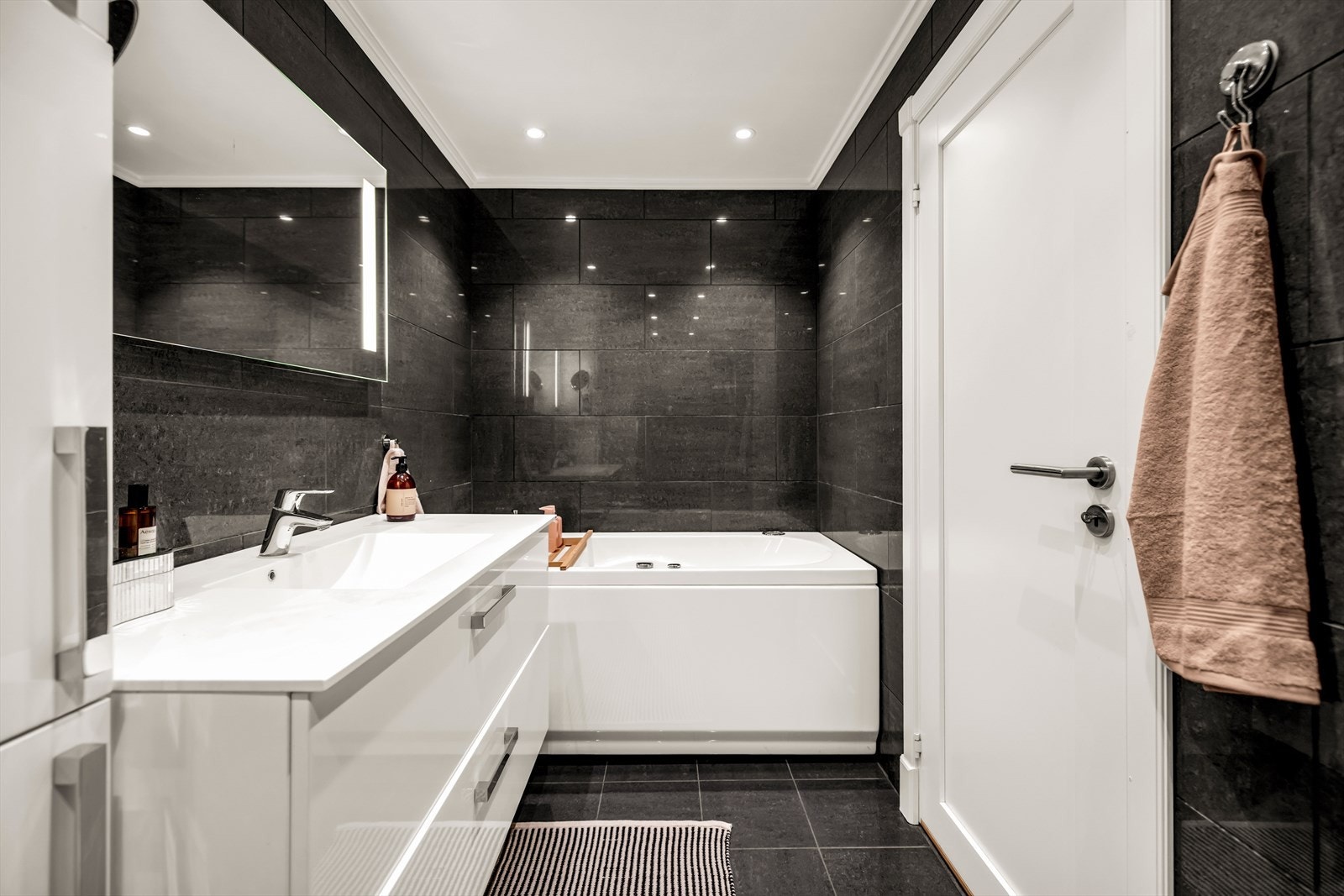 Badet er innredet med vegghengt toalett, servant med underskap, speil med lys, dusjhjørne med svingbare glassdører samt badekar. Galleribilde