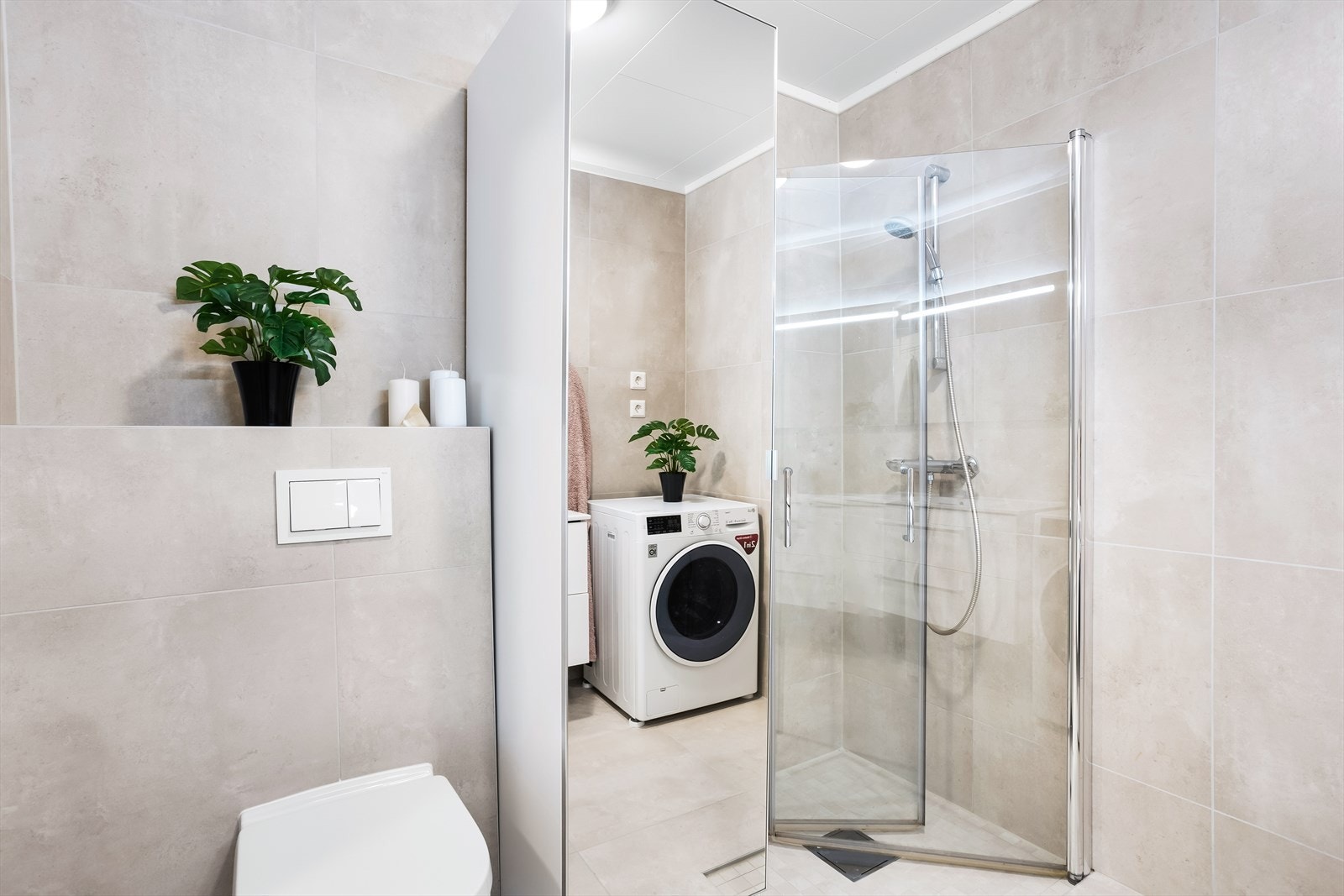 Badet har hvit servantinnredning, speil, toalett, nedsenket dusjhjørne med glassdører og opplegg for vaskemaskin. Galleribilde