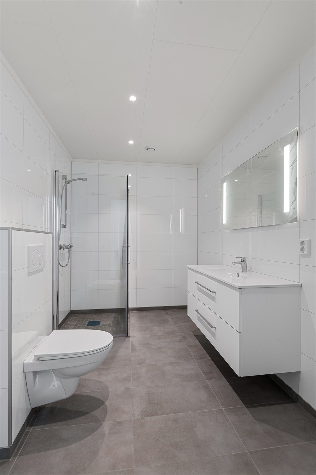 Videre er badet utstyrt med dusjhjørne med innfellbare dusjvegger og vegghengt toalett. Galleribilde