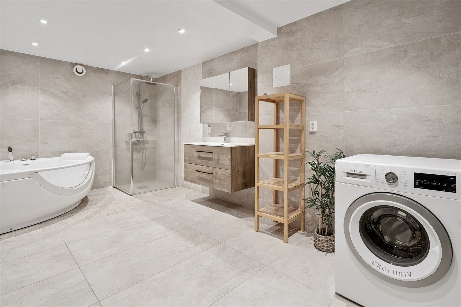 Lekkert flislagt bad med badekar, dusjnisje, baderomsinnredning og opplegg for vaskemaskin Galleribilde