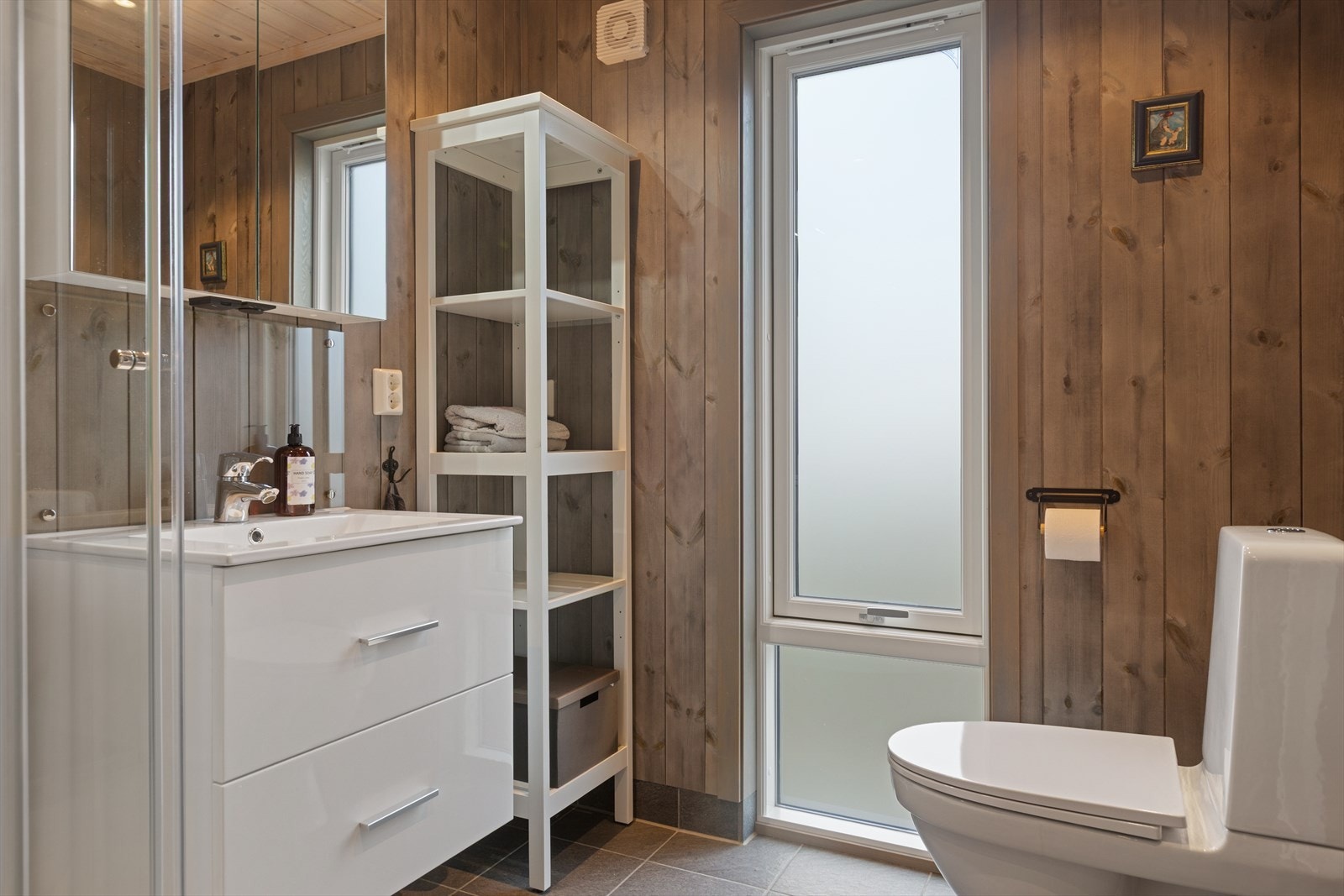 Hyttas bad er delikat med flislagt gulv og varmekabler. Lys baderomsinnredning med store skuffer og heldekkende servantplate, samt overskap med speildører. Galleribilde