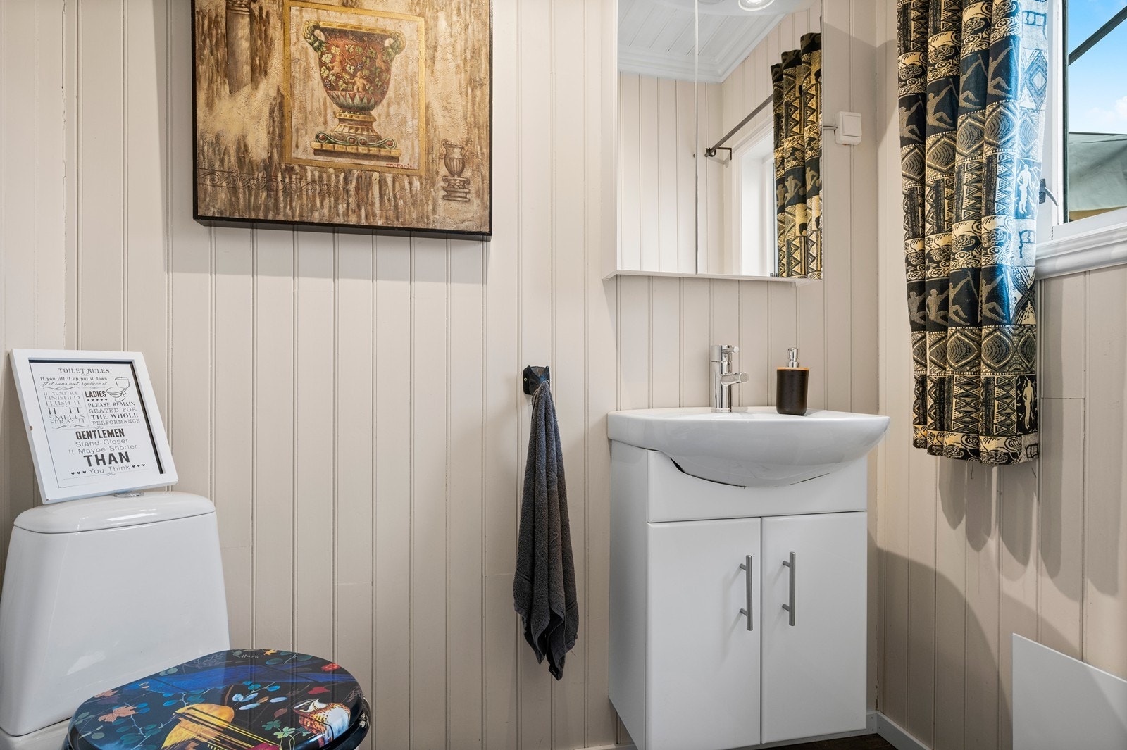 I entréen er det et praktisk toalettrom/gjestetoalett, med malt panel på veggene og laminat på gulvet. Det er innredet med nedfelt servant i skapinnredning med speilskap over, samt gulvmontert wc Galleribilde