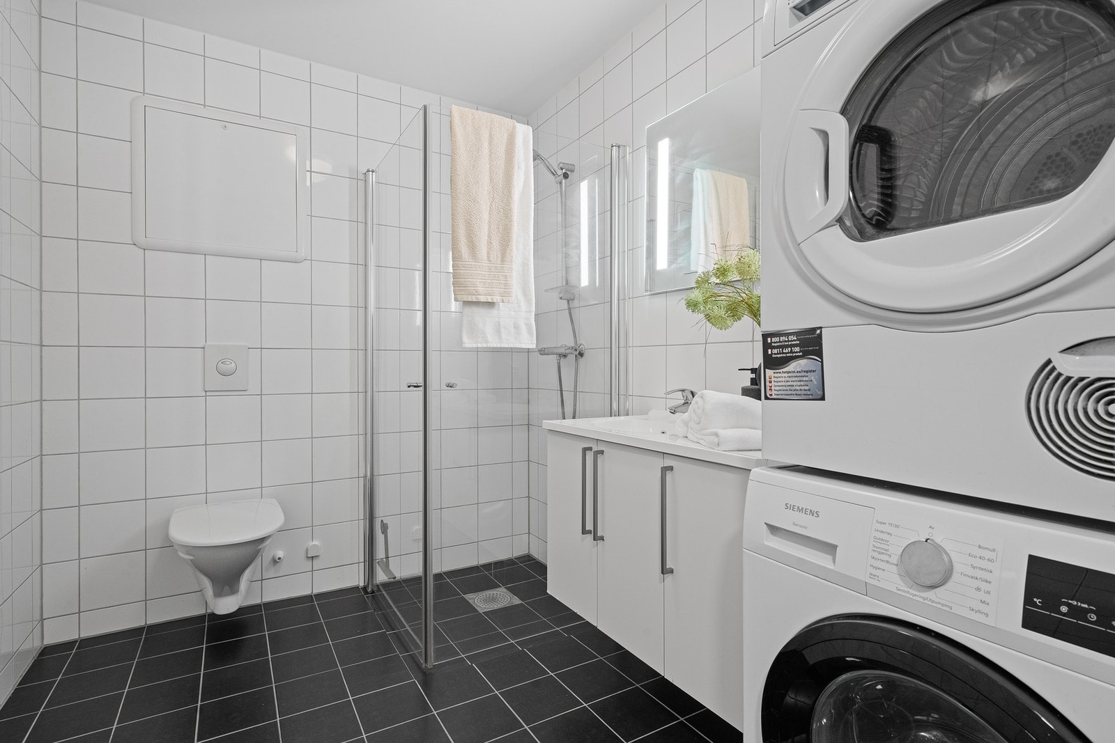 Dusjhjørne, vegghengt toalett, servantmøbel og opplegg for vaskemaskin/tørketrommel. Galleribilde