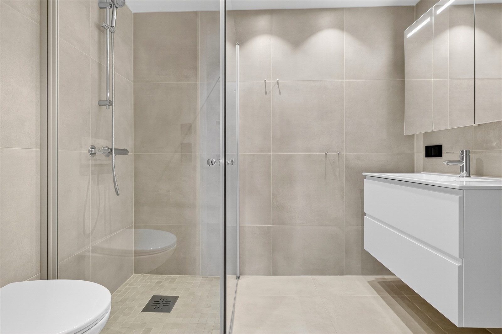 Himlingen er malt og har spotbelysning. Innredningen består av heldekkende servant med skuffer og skap, speil med integrert lys, vegghengt toalett og dusjhjørne med glassvegger. Galleribilde