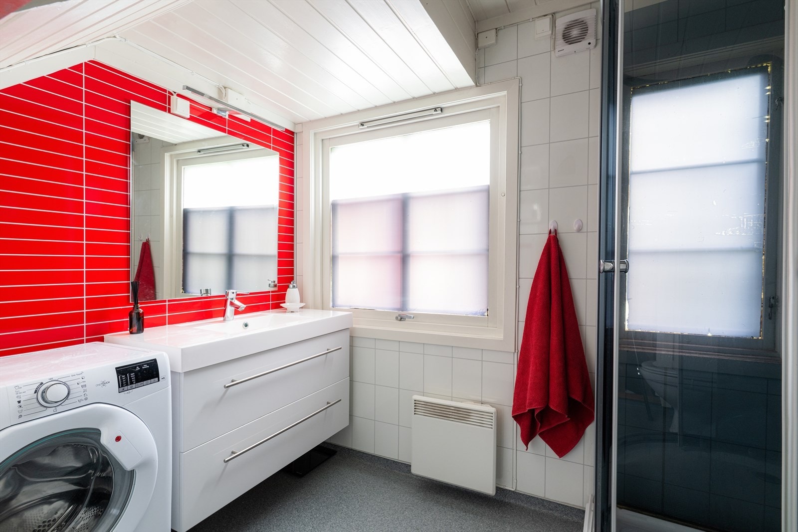 Badet med vaskeromfunksjoner har belegg på gulvet og baderomsplater på veggoverflatene. Her er det innredning med dype skuffer og heldekkende servant, samt speil på vegg, dusjkabinett og toalett. Opplegg for og plass til vaskemaskin. Galleribilde