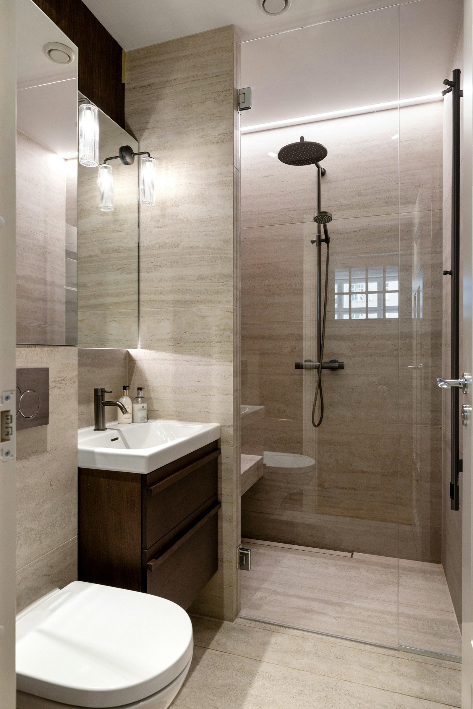 Dusjen er utstyrt med både regnfalldusj og praktisk benk som gir spafølelse. Lekre fliser og moderne armaturer setter en eksklusiv tone, mens de store speilflatene bidrar til å skape en lys og romslig følelse. Galleribilde