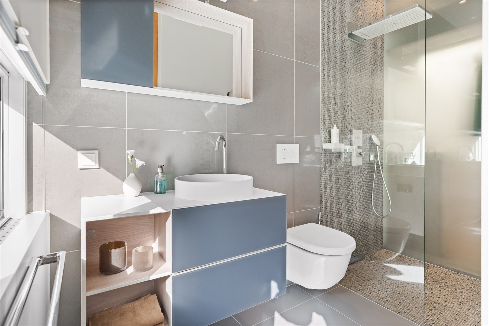 Soverommets bad er utstyrt med vegghengt toalett, servant med praktiske skuffer, overskap med speil, og et elegant dusjhjørne med glassdører - alt designet for både funksjon og estetikk. Galleribilde