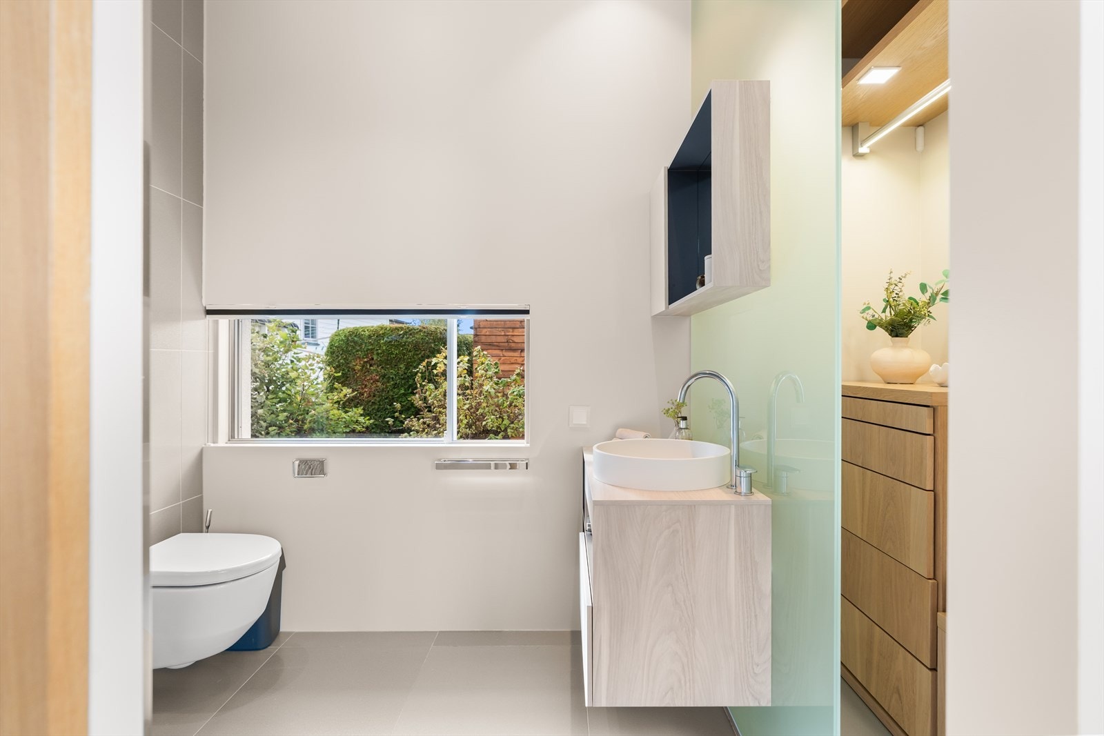 Baderommet er utstyrt med vegghengt toalett, servant med praktiske skuffer, overskap med speil, og et elegant dusjhjørne med glassdører. Galleribilde