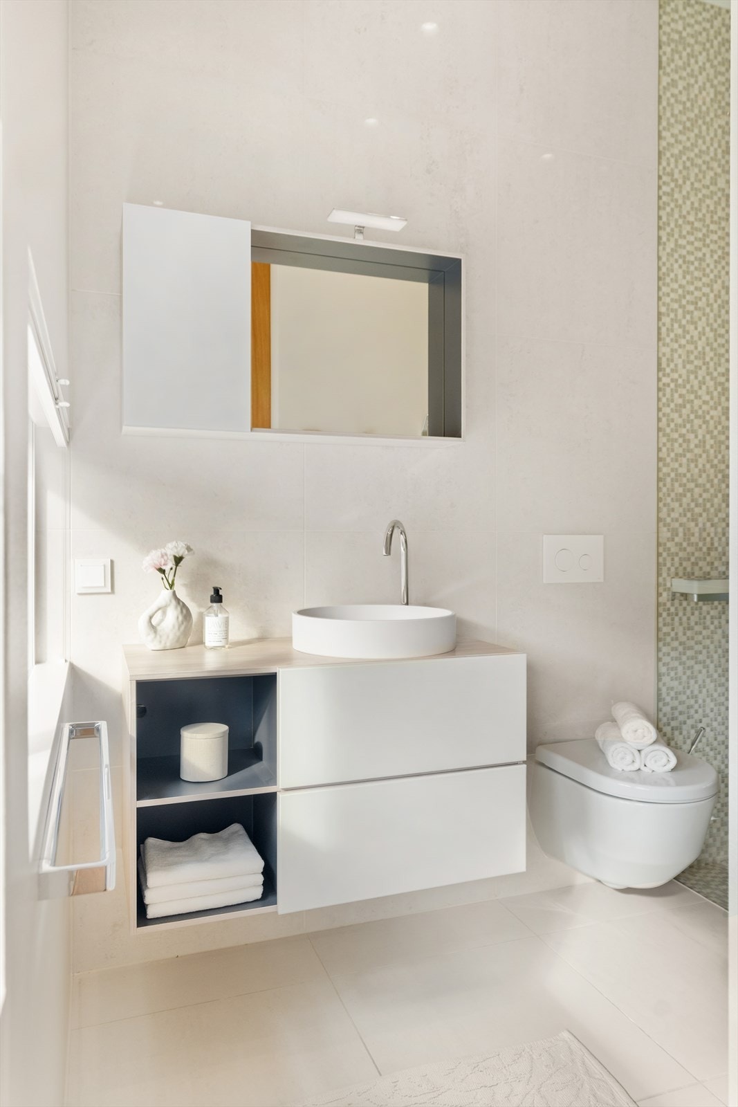 Soverommets bad er utstyrt med vegghengt toalett, servant med praktiske skuffer, overskap med speil, og et elegant dusjhjørne med glassdører. Galleribilde