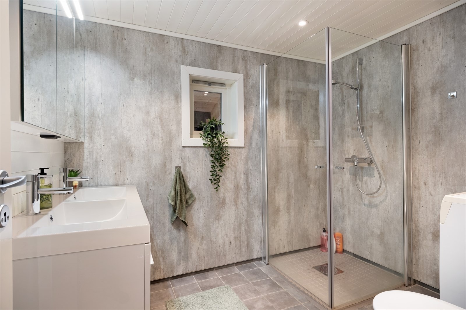 Badet er utstyrt med dobbeltservant med underskåp, overskåp med spegel, toalett, dusjhjørne med glasdører og opplegg for vaskemaskin. Galleribilde