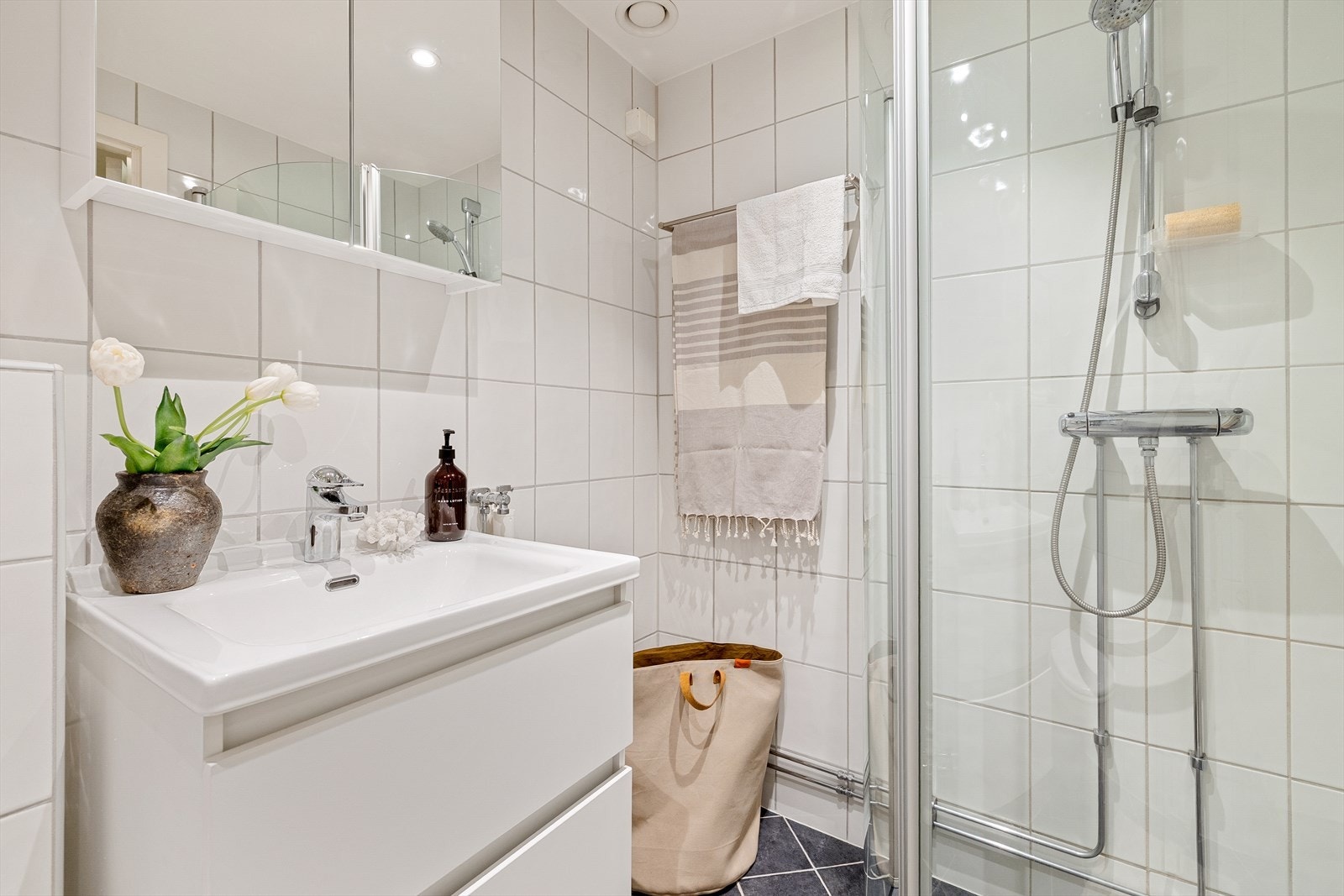 Badet er utstyrt med vegghengt toalett, servantinnredning til oppbevaring med servant, ettgreps blandebatteri, blandebatteri/dusjarmatur, dusjdører i glass. Det er plass og opplegg for vaskemaskin Galleribilde