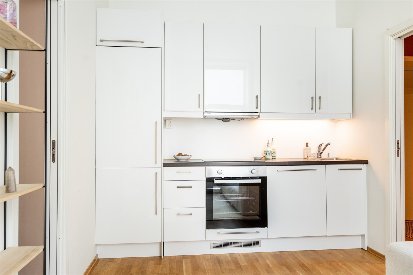 Det er belysning via lysarmatur under overskap, mekanisk avtrekk over komfyr og integrerte hvitevarer som platetopp, stekeovn (2025), oppvaskmaskin og kjøle-/fryseskap. Galleribilde