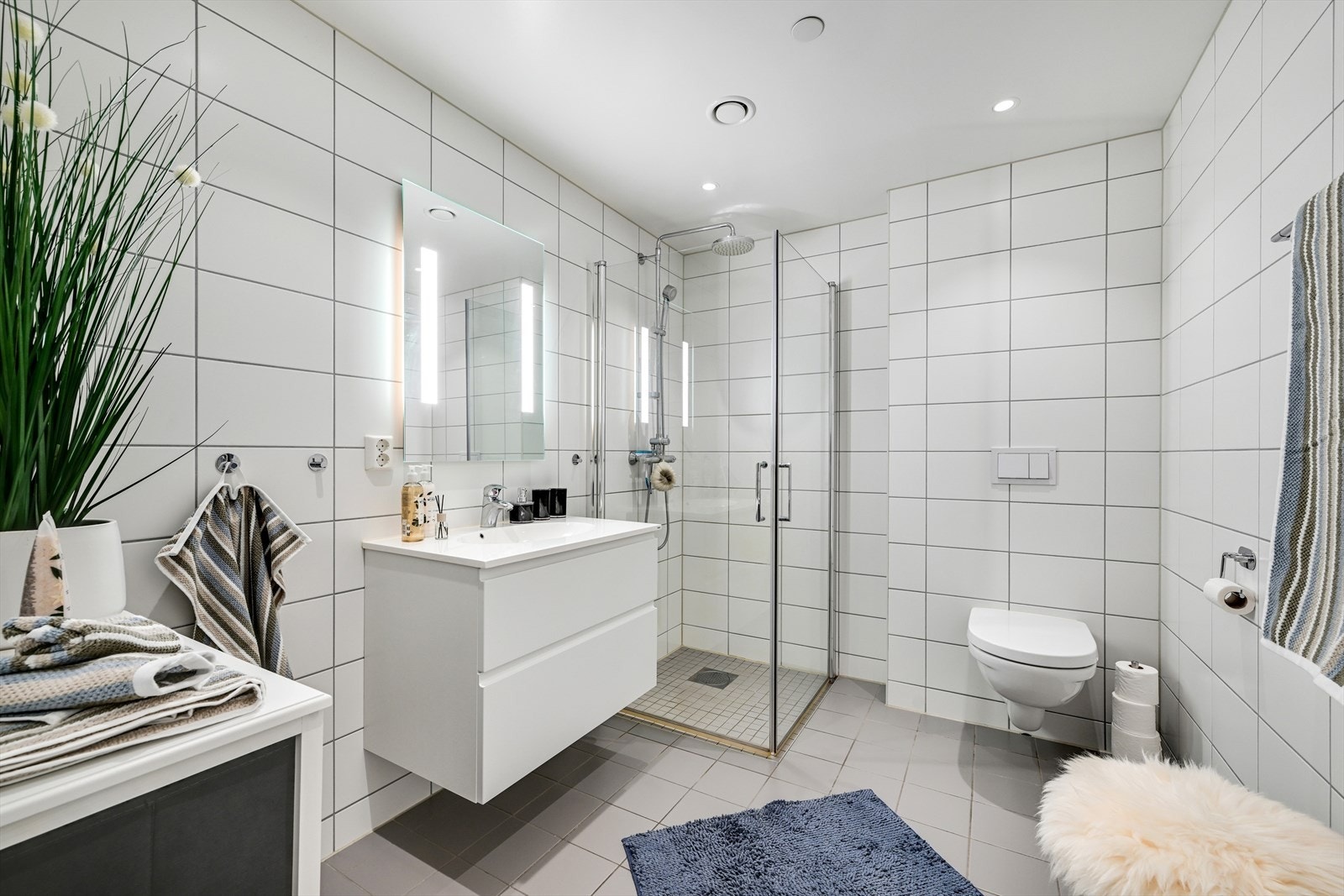 Fliselagt bad/wc med dusjhjørne, servant med skuffer under, speil med integrert lys og vegghengt toalett Galleribilde