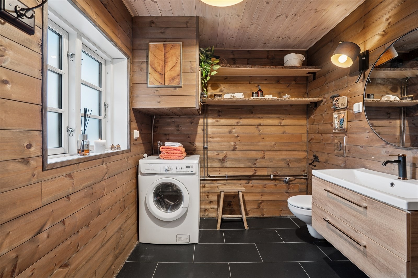 Baderom med veggmontert toalett og opplegg for vaskemaskin. Flislagt gulv med elektriske varmekabler. Galleribilde