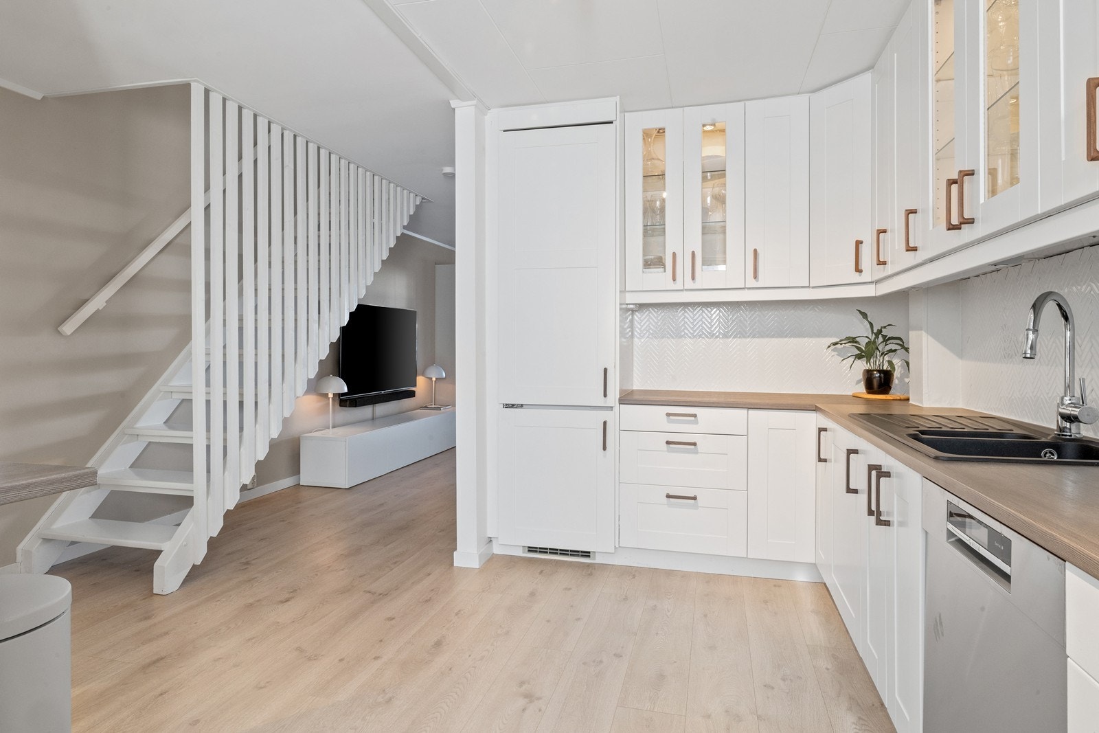 Innredningen har lyse, profilerte fronter, vitrineskap med glass, mørk benkeplate i laminat, og dobbel vaske- og skyllekum. Galleribilde