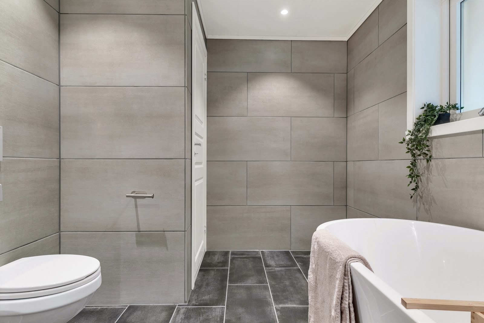 Badet er helfliset og inneholder vegghengt toalett, badekar, helstøpt servant og skuffer under servant med slette fronter i tillegg til varmekabler Galleribilde