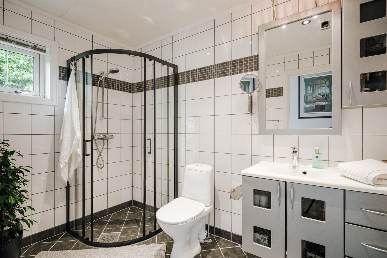 Badet i hoveddelens 2. etasje har flislagt gulv og vegger. Rommet er innredet med servantskap med nedfelt servant, speil med lys over, gulvmontert klosett og dusjnisje med herdet glass. Varmekablene fungerer ikke. Galleribilde