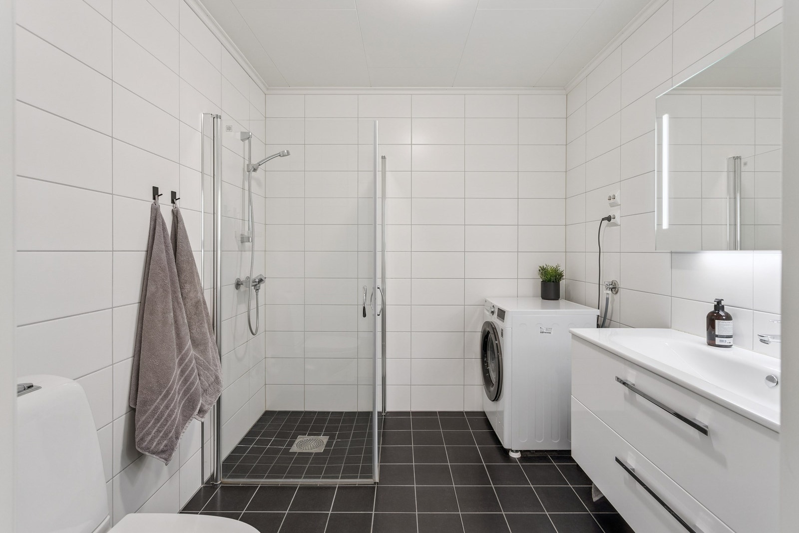 Badet er helfliset og utstyrt med dusjhjørne, vegghengt toalett og opplegg for vaskemaskin. Galleribilde