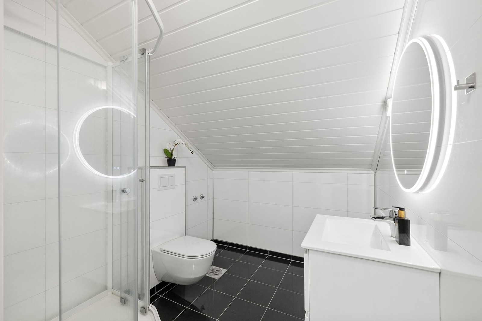 Bad med fliser på gulv med gulvvarme og baderomsplater på vegger. Innredningen består av et underskap,, servant, speil med lys og stikk. Galleribilde