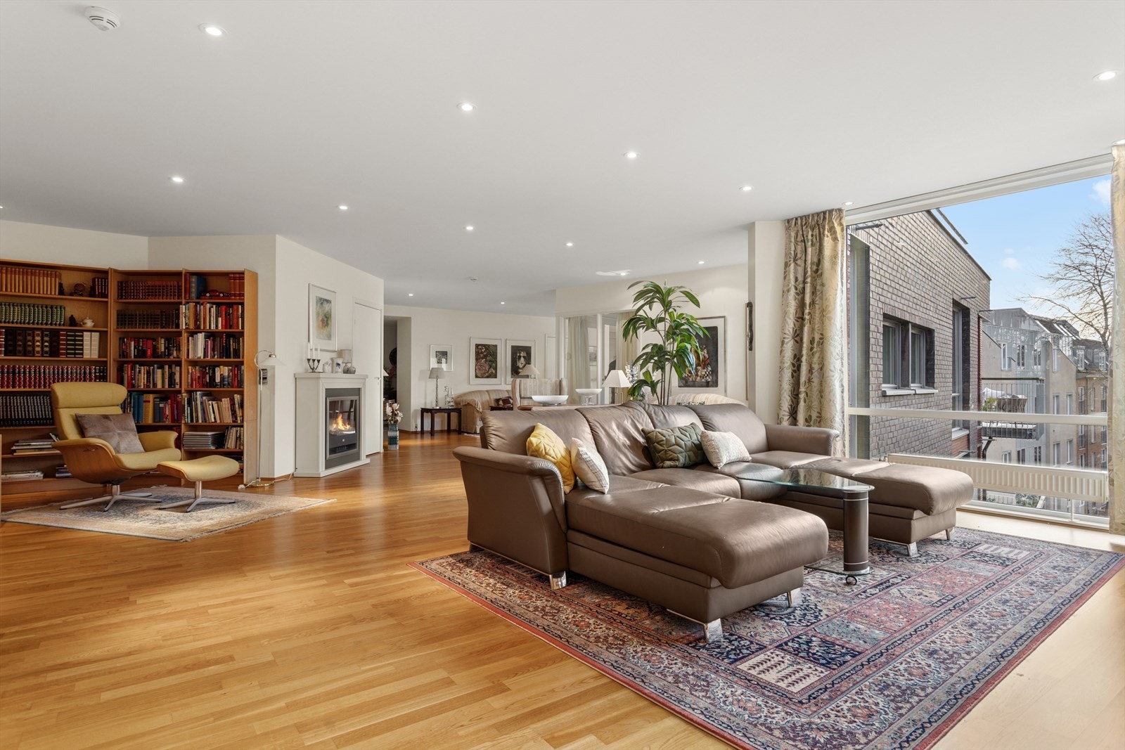 Store vindusflater gir utsyn mot nærliggende bygninger og hageområde. Galleribilde