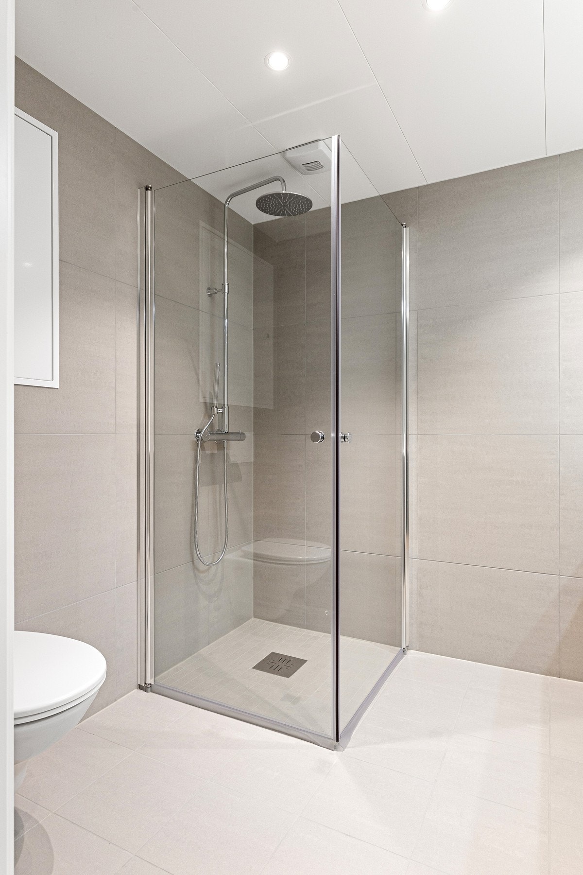 Badet er innredet med vegghengt toalett, baderomsinnredning med benkeplate og integrert servant, samt dusjhjørne med regnfallsdusj og glassdører. Galleribilde