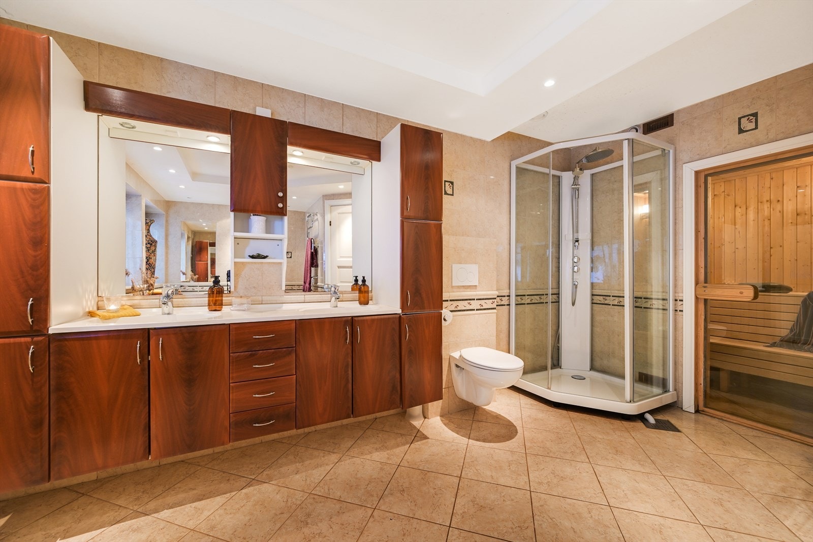 Innholdsrik baderomsinnredning med to helstøpte servanter, innebygget badekar, vegghengt toalett og dusjkabinett. Videre adkomst in i badstuen. Galleribilde