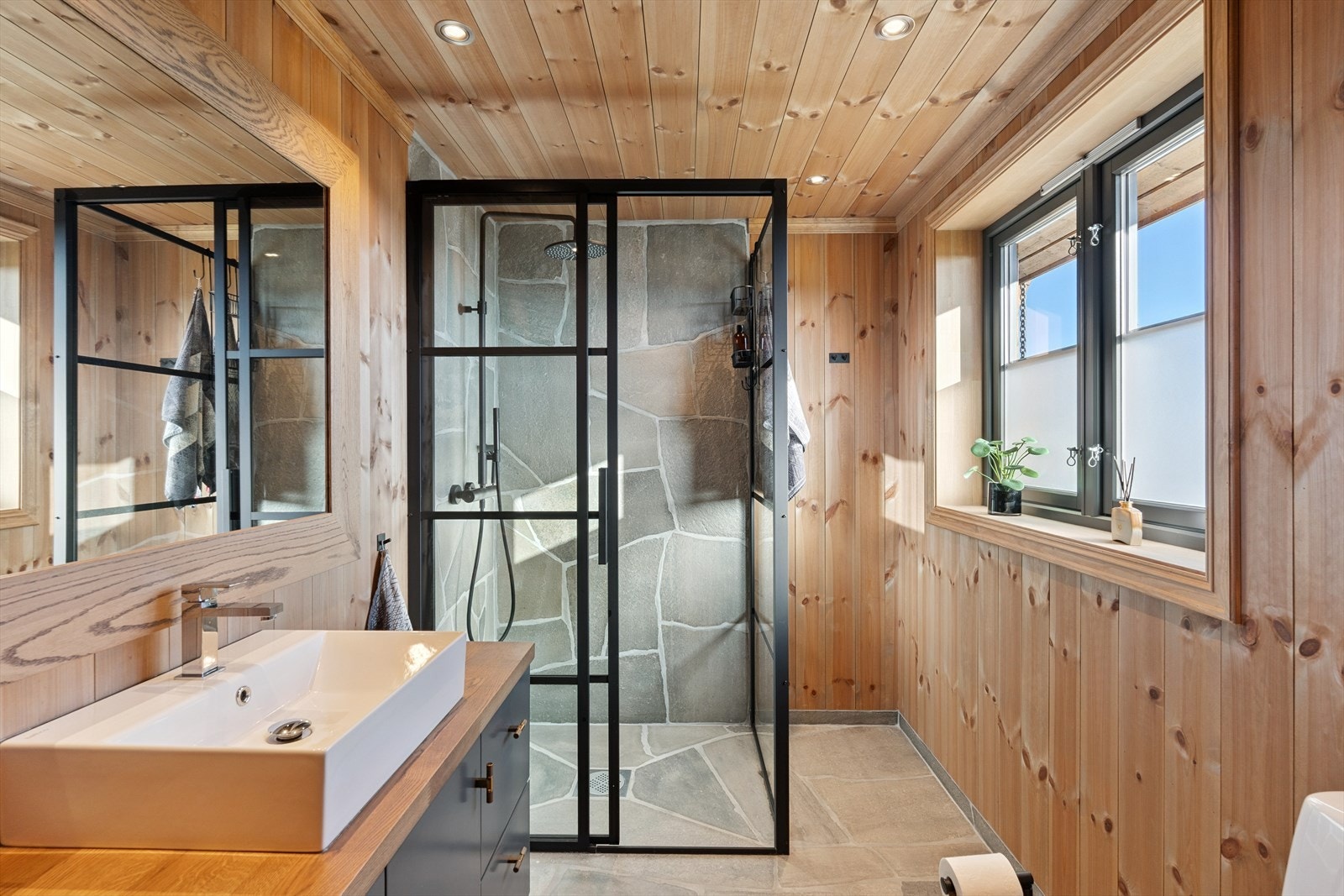 Badet er delikat med servantskap av malte/laminerte trefiberplater med skap og skufferekke, benkeplate i eik, speil, toalett samt dusjhjørne med skifer- og glassvegger. Varmekabler i gulvet. Galleribilde