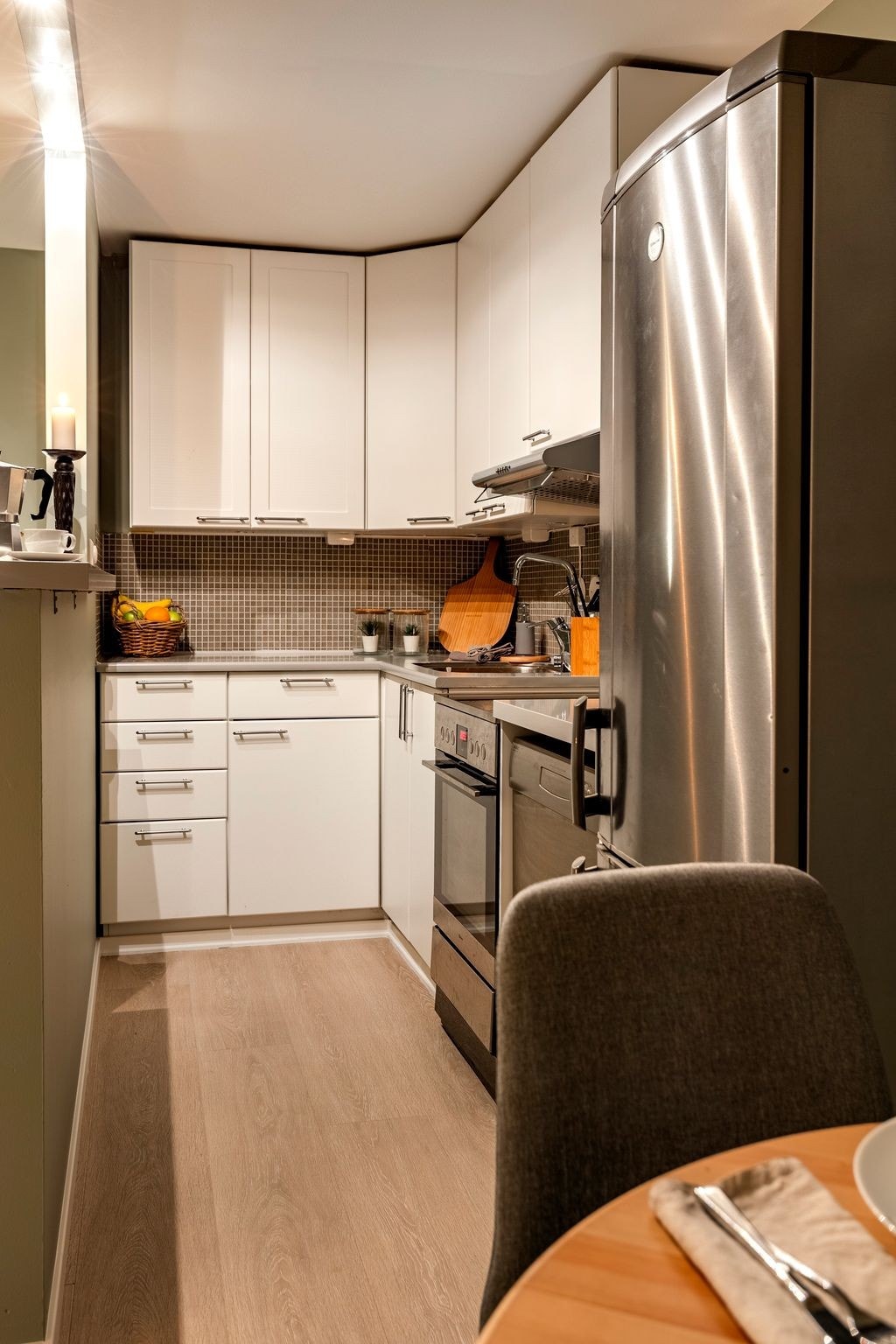 Mellom benk og overskap er det brune mosaikkfliser. Benkeplaten er i laminat, med stålkum og benkebelysning. Det er montert kullfilterventilator over kokesonen, og det finnes opplegg for oppvaskmaskin samt plass til kjøleskap. Galleribilde