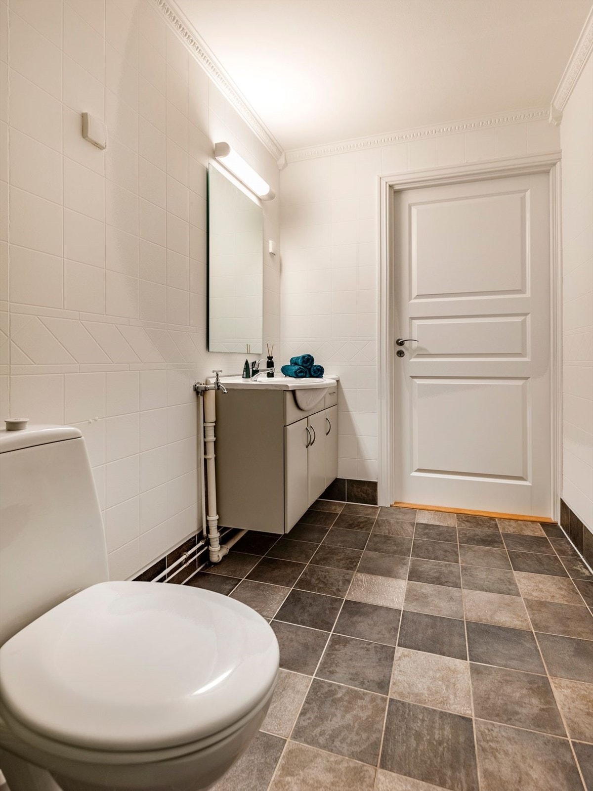 Rommet inneholder speil med belysning, et servantskap med beige fronter, gulvmontert toalett og dusjkabinett. Galleribilde