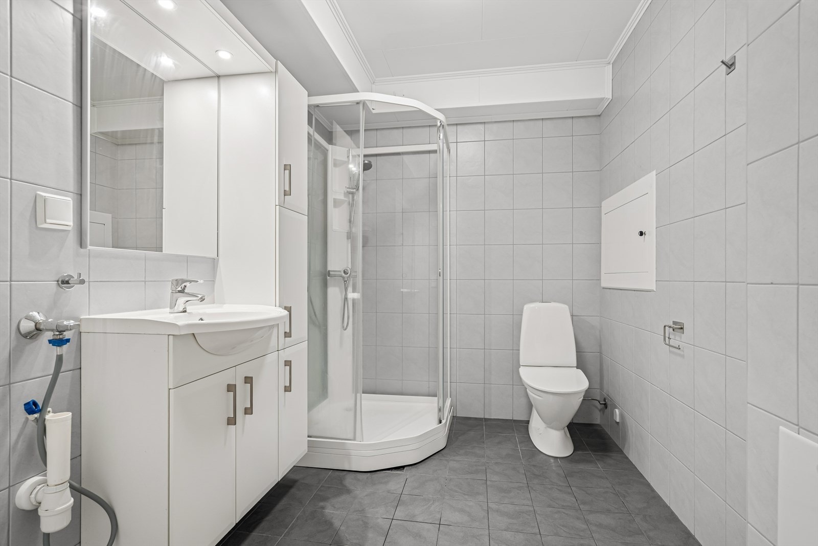 Badet er stilrent med grå gulvfliser og lyse veggfliser Galleribilde