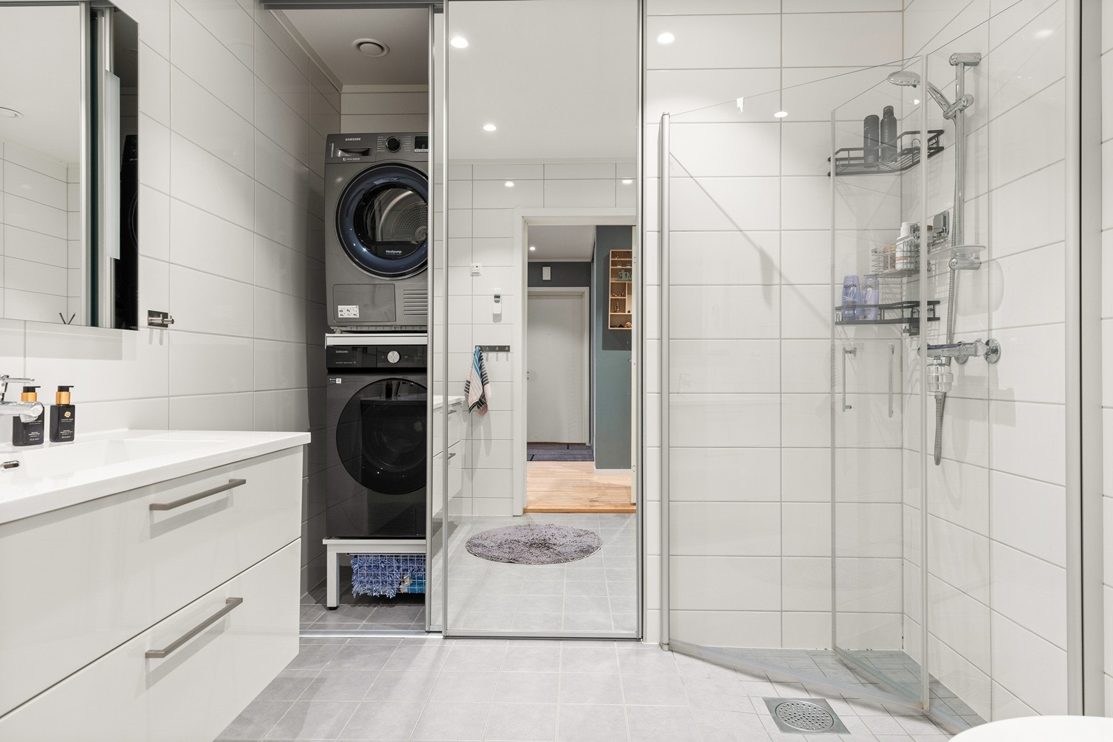 Baderommet har en standard fra byggeåret 2018, og er delikat helfliset. Egen sone med opplegg for vaskemaskin og tørketrommel, skjermet bak skyvedører med speilfronter. Videre er det dusjhjørne med innfellbare dører, og vegghengt wc Galleribilde