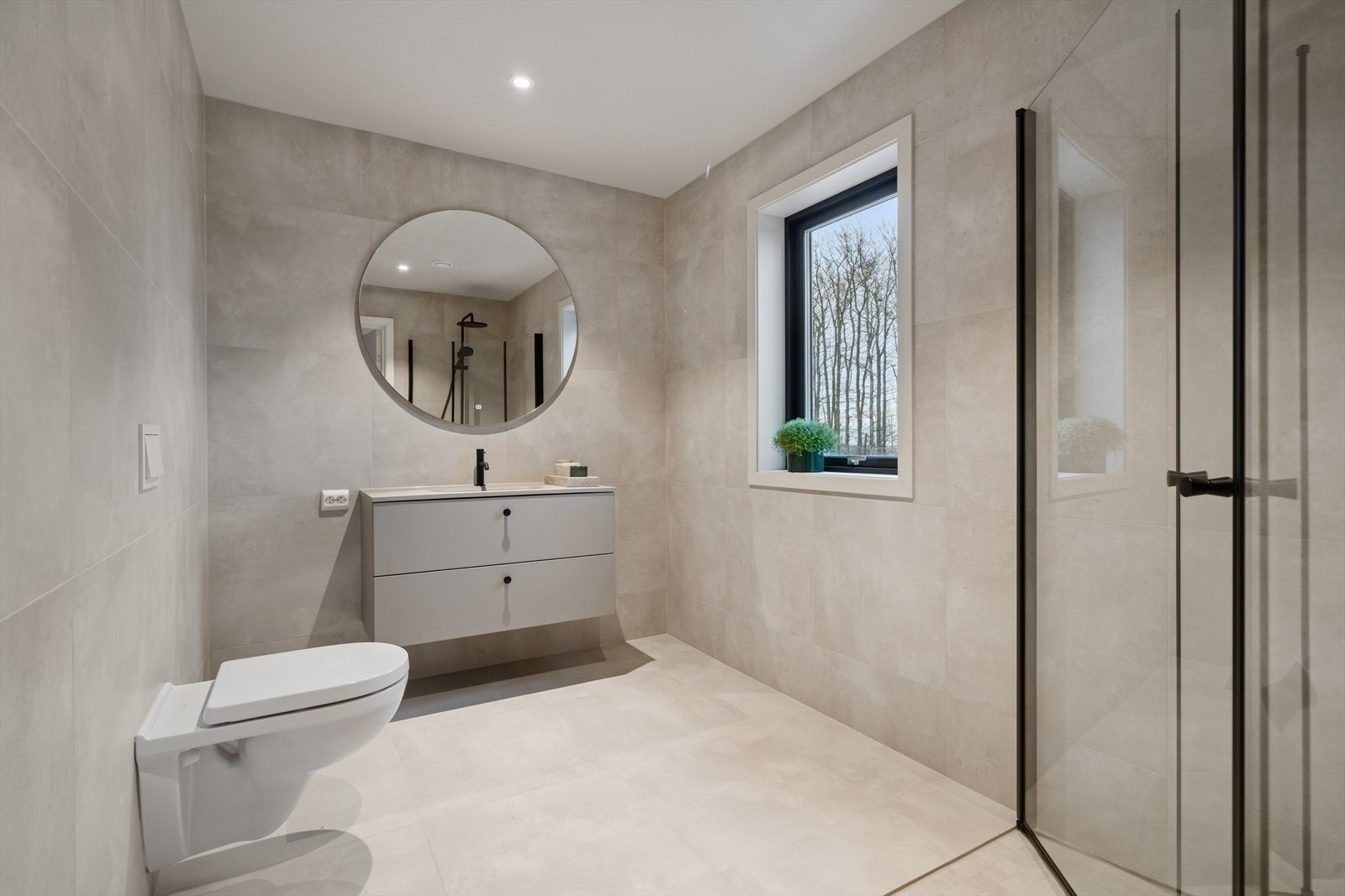 Badet i 2. etasje innehar servantinnredning, rundt speil, vegghengt toalett og dusjhjørne. Galleribilde