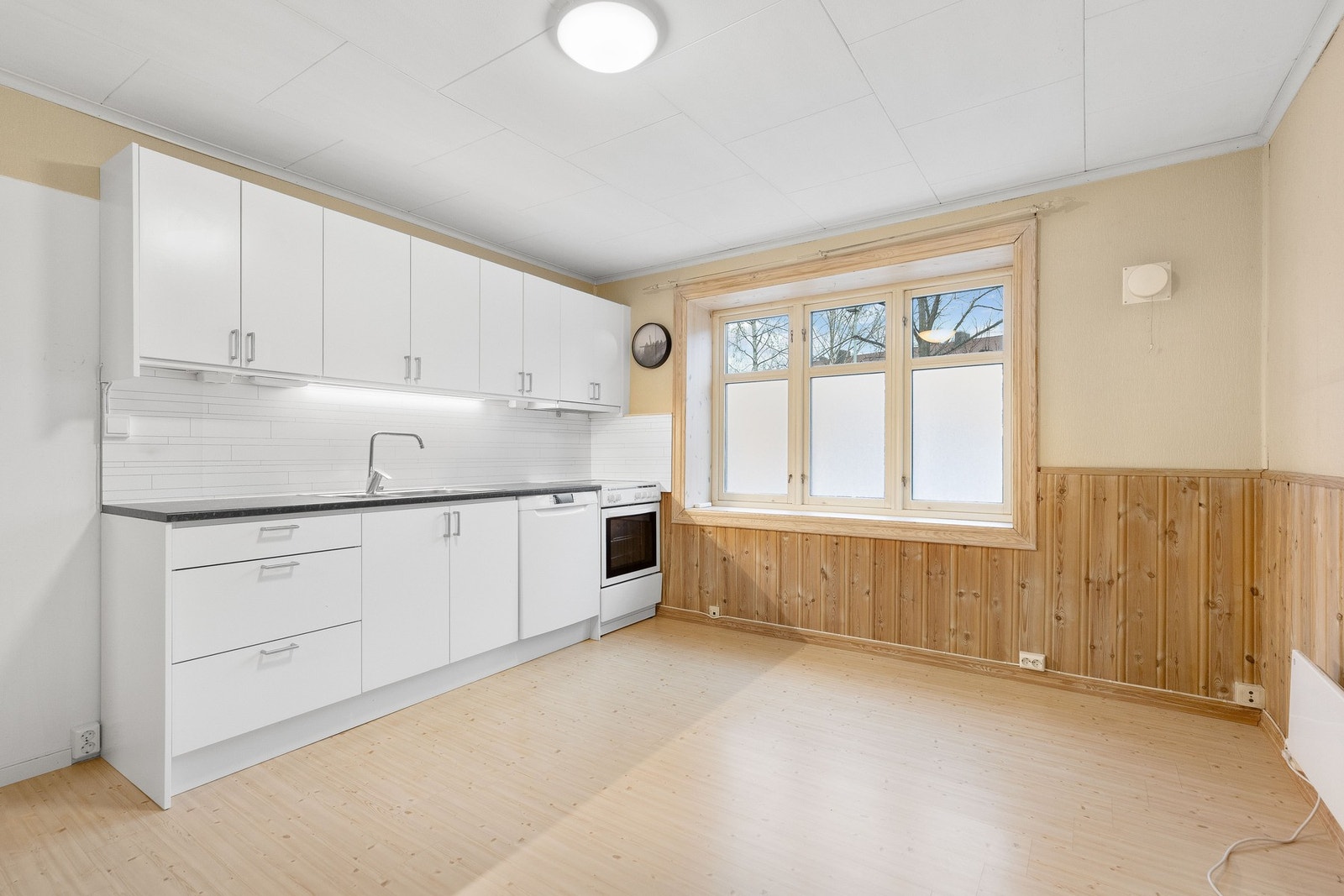 Lyst kjøkken med hvite skap, lys benkeplate og stort vindu som gir godt med naturlig lys. Galleribilde