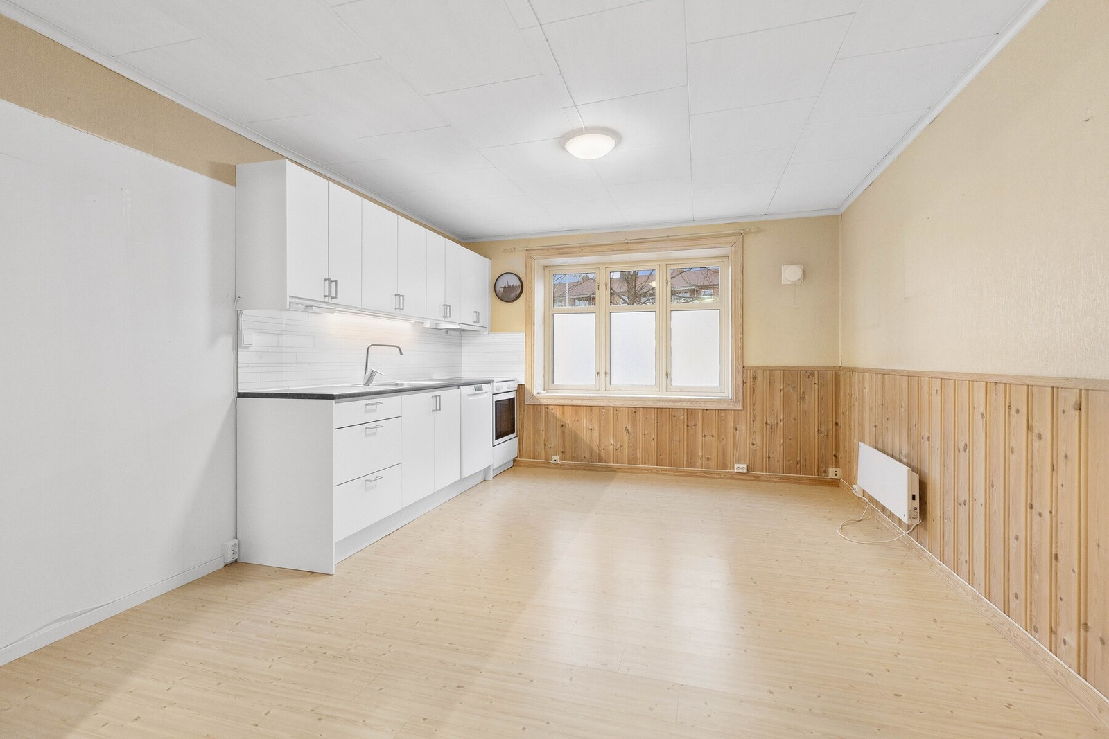 Lyst kjøkken med hvite skap, laminatgulv og panel på veggene. Store vinduer gir naturlig lysinnslipp. Galleribilde