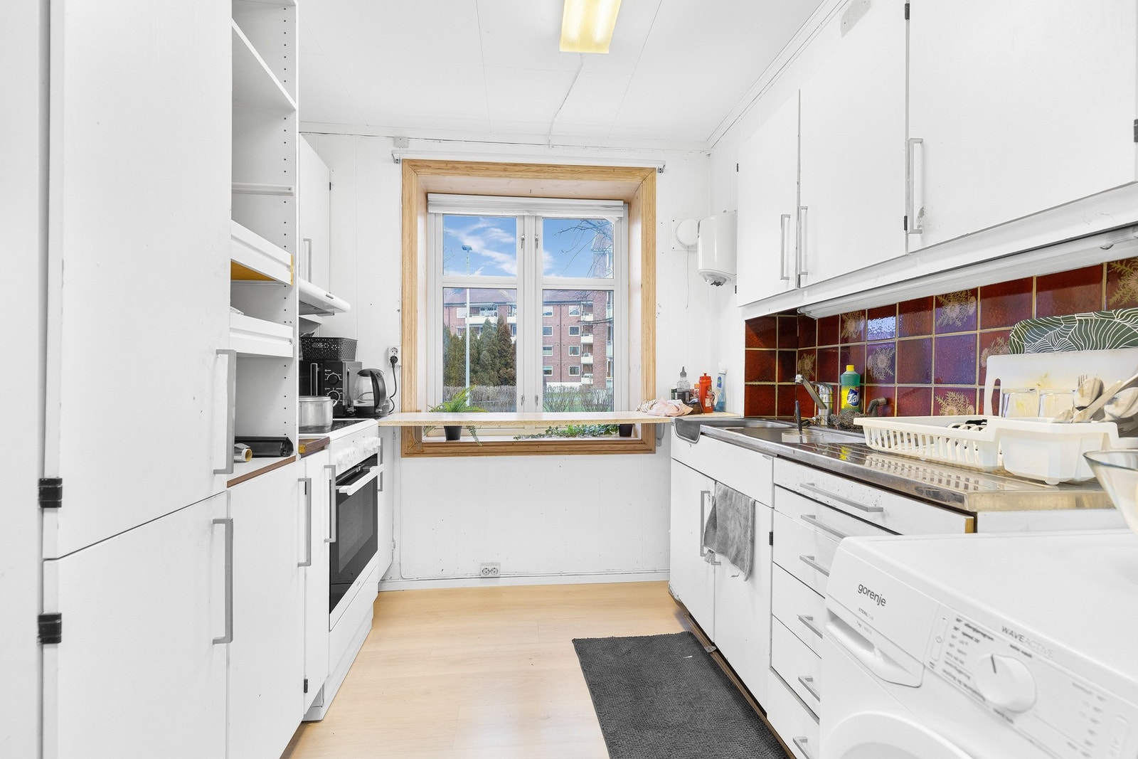 Det ene kjøkkenet i 1. etasje har hvite skap og skuffer, og utsikt mot nabolaget. Galleribilde